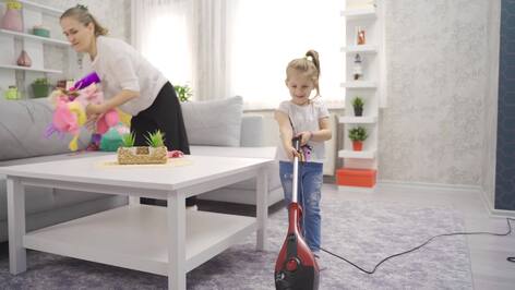 Cute little girl helping her mother at home vacuuming the house. Little girl cleans the house and cleans the floors with the vacuum cleaner in the house.